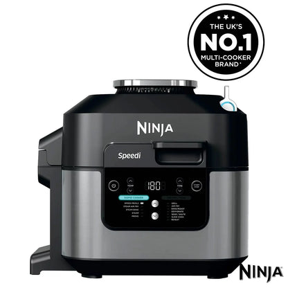 Front view of the black steel Ninja Speedi ON500UK multi cooker sitting on a dark kitchen countertop with its lid open, displaying cooked chicken breasts and steamed vegetables inside the inner pot.