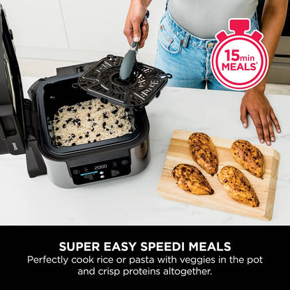 Front view of the black steel Ninja Speedi ON500UK multi cooker sitting on a dark kitchen countertop with its lid open, displaying cooked chicken breasts and steamed vegetables inside the inner pot.