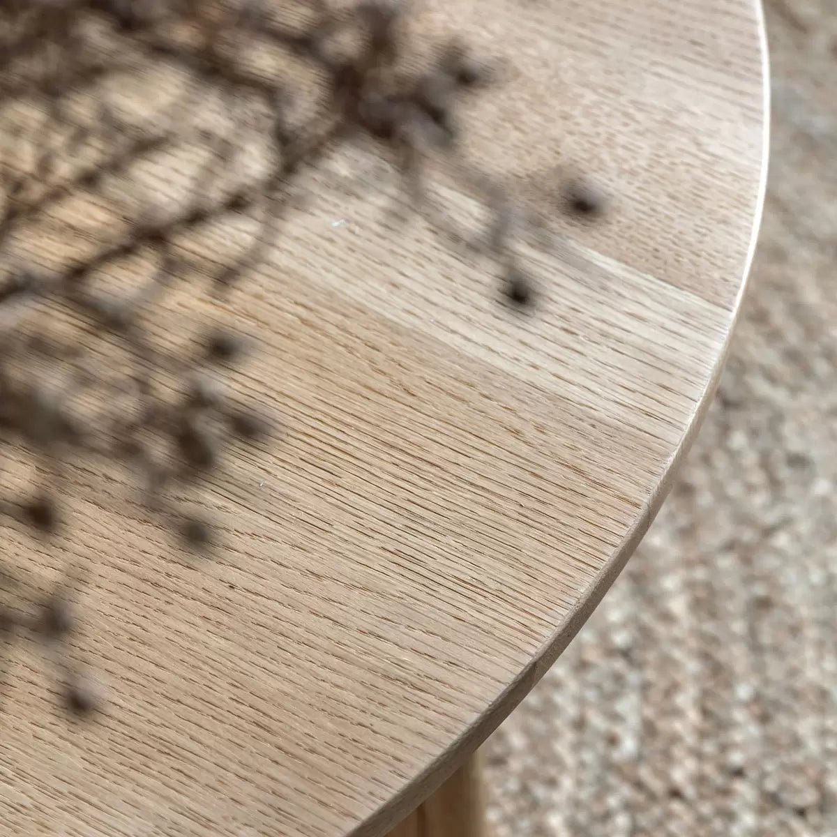 Natural light oak round coffee table featuring a geometric crossover timber base styled on a textured rug in a bright, minimalist modern living room.