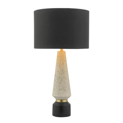 Front view of the Onora table lamp featuring a cylindrical black and gold flecked terrazzo base, topped with a black faux silk drum shade on a concrete sideboard.