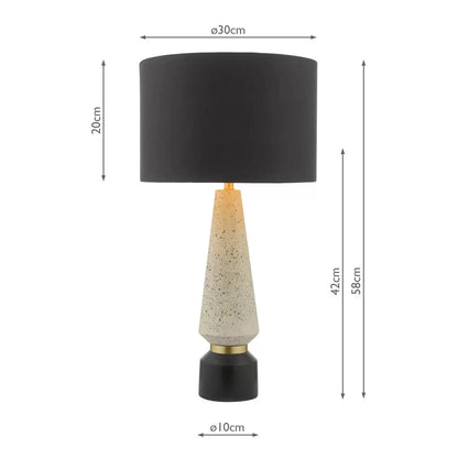 Front view of the Onora table lamp featuring a cylindrical black and gold flecked terrazzo base, topped with a black faux silk drum shade on a concrete sideboard.
