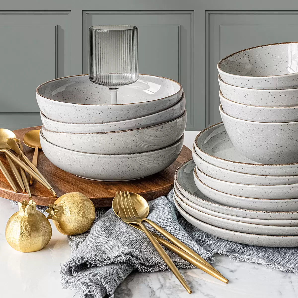 Over & Back 16 piece stoneware dinnerware set in light grey stacked neatly on a rustic wooden dining table