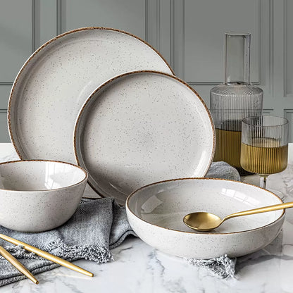 Over & Back 16 piece stoneware dinnerware set in light grey stacked neatly on a rustic wooden dining table