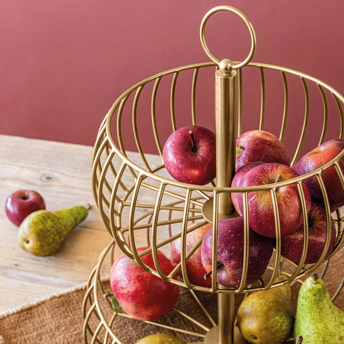 Over & Back 2-Tier brushed gold metal basket displayed on a kitchen counter filled with fresh fruit.