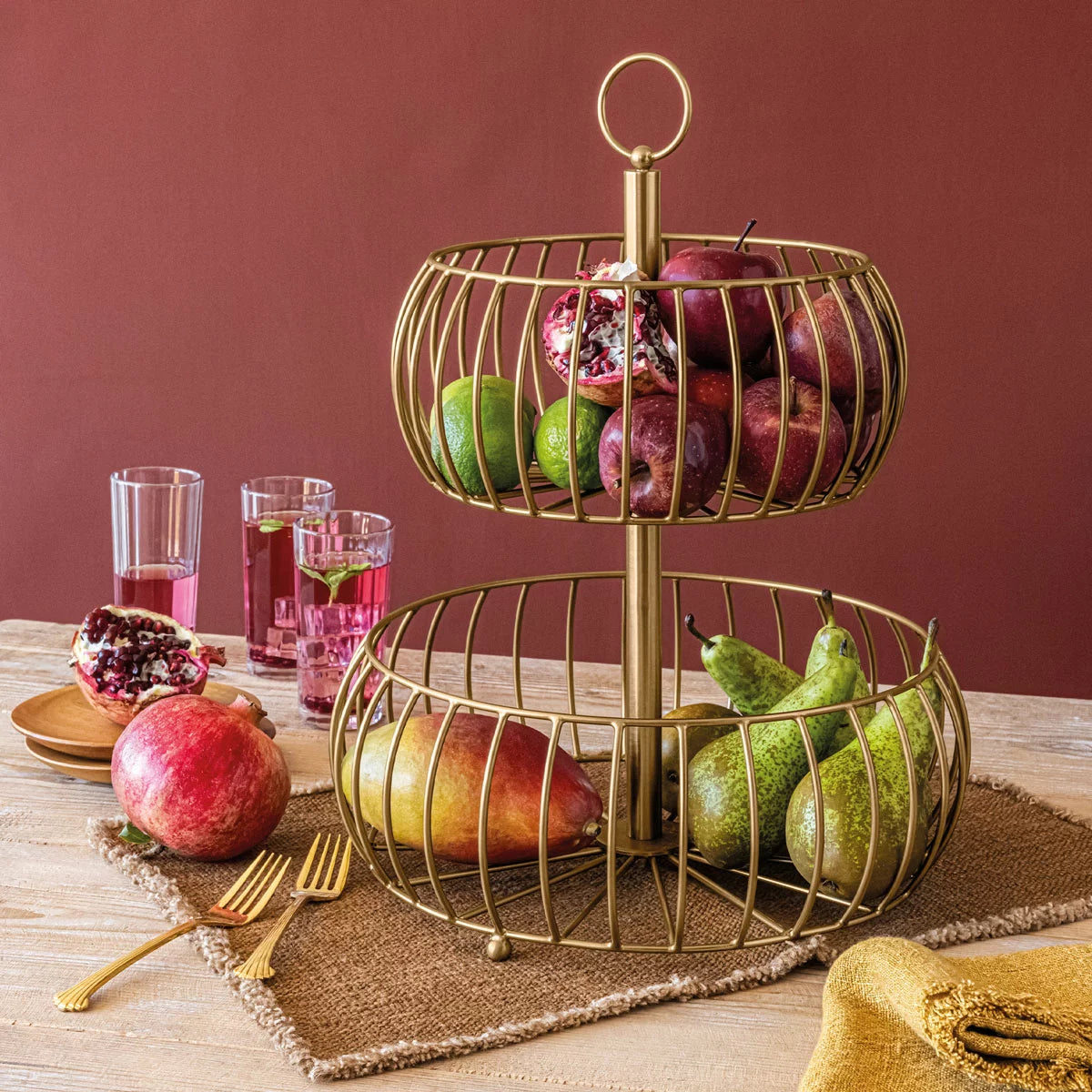 Over & Back 2-Tier brushed gold metal basket displayed on a kitchen counter filled with fresh fruit.