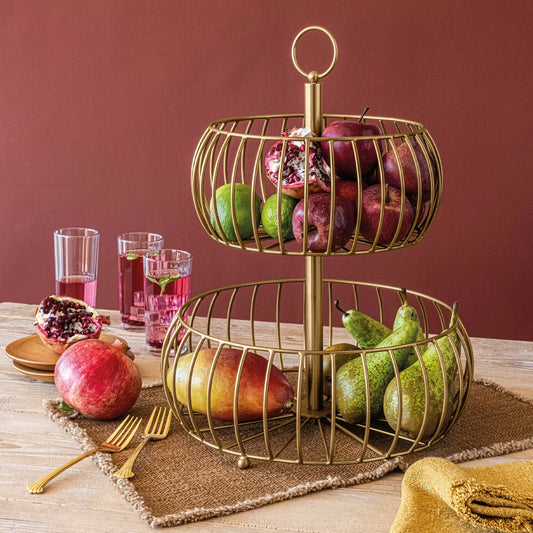 Over & Back 2-Tier brushed gold metal basket displayed on a kitchen counter filled with fresh fruit.