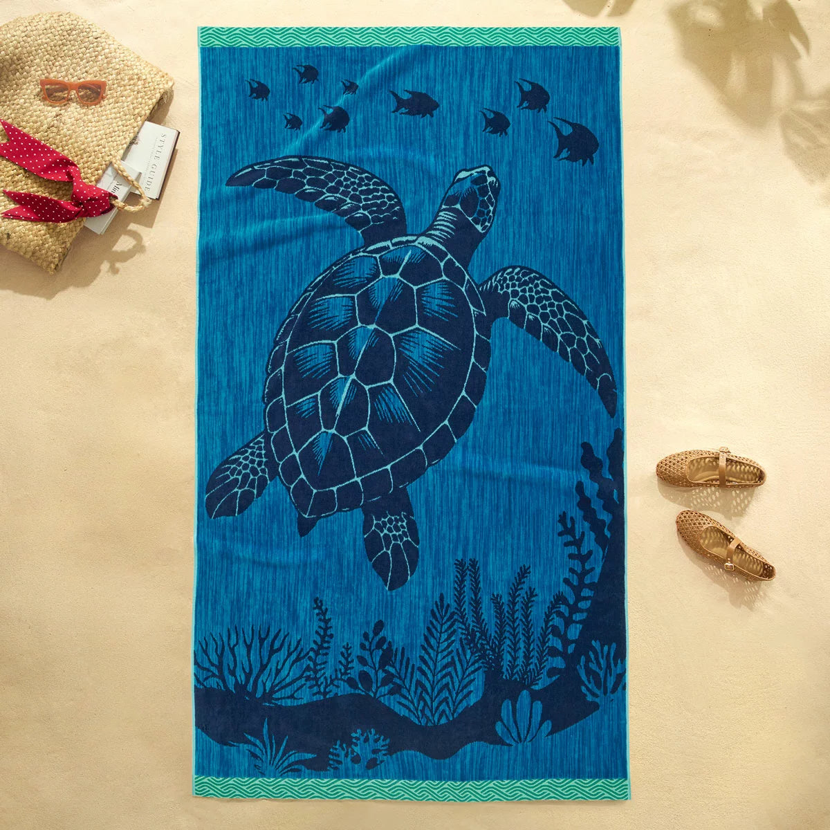 Flat lay view of the plush 500 GSM oversized 100 percent cotton jacquard beach towel spread out on golden sand.