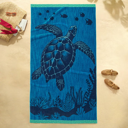 Flat lay view of the plush 500 GSM oversized 100 percent cotton jacquard beach towel spread out on golden sand.