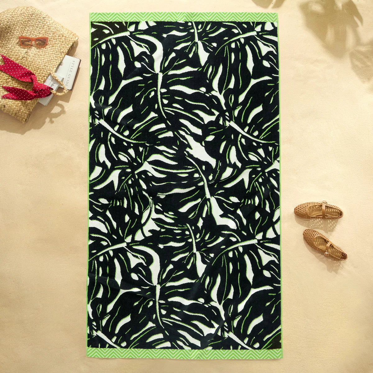 Flat lay view of the plush 500 GSM oversized 100 percent cotton jacquard beach towel spread out on golden sand.
