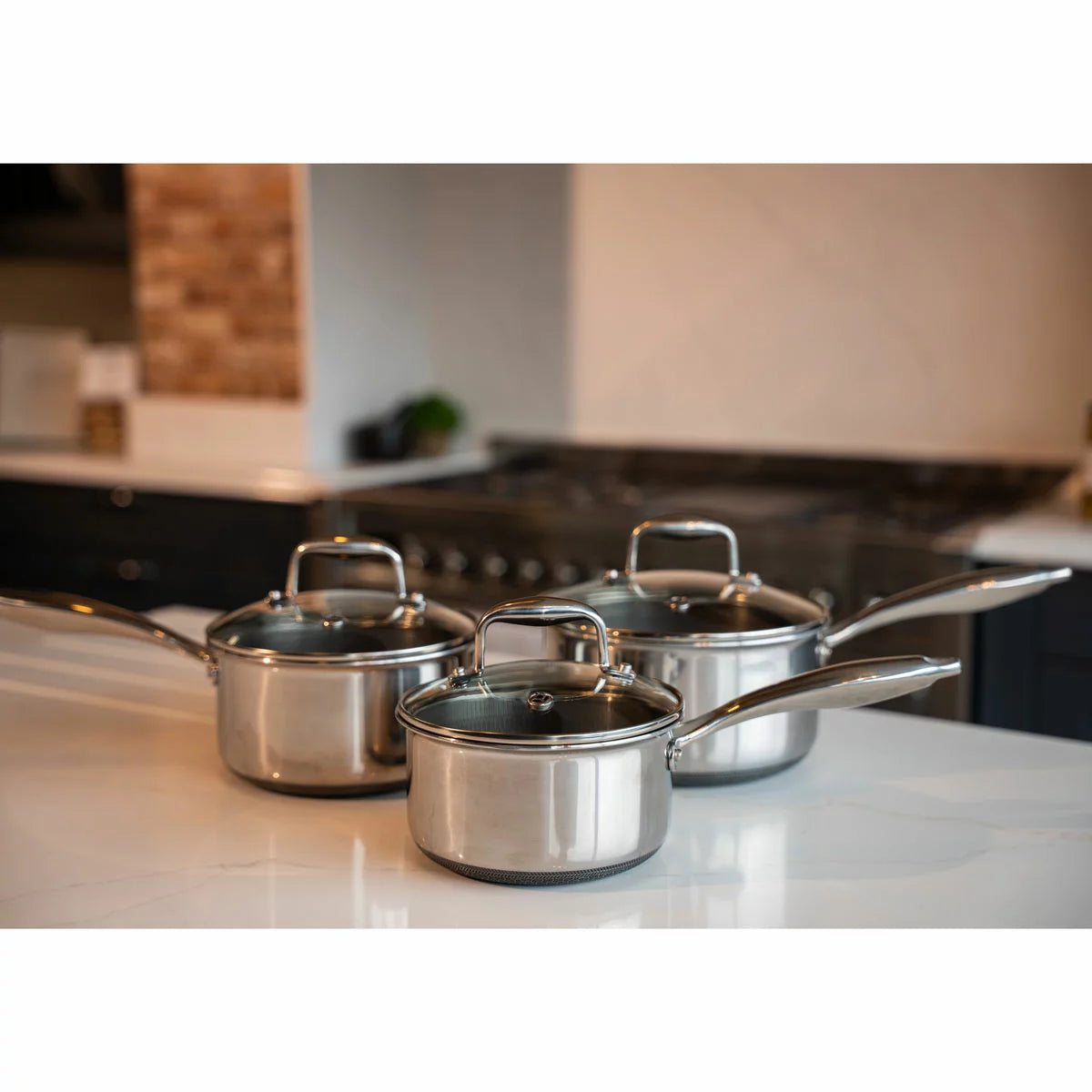 A high-end kitchen display featuring the PRO STEEL Fusion 6 piece saucepan set, showcasing the sleek stainless steel exteriors, glass lids, and the durable hybrid cooking surfaces.