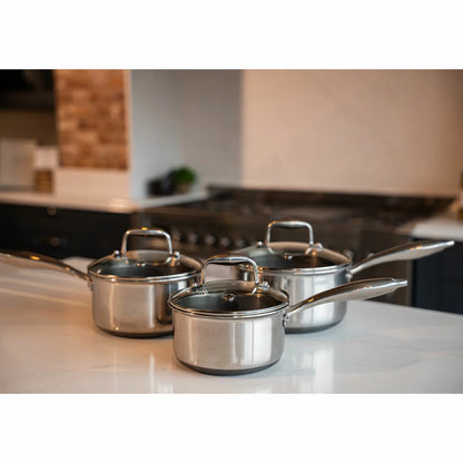 A high-end kitchen display featuring the PRO STEEL Fusion 6 piece saucepan set, showcasing the sleek stainless steel exteriors, glass lids, and the durable hybrid cooking surfaces.
