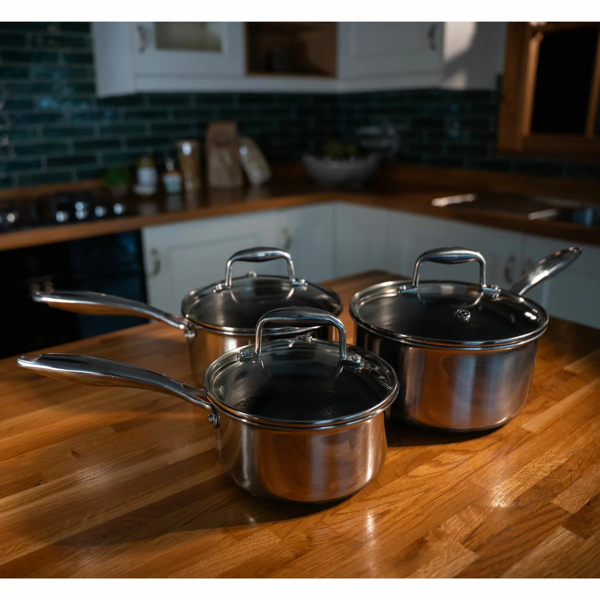 A high-end kitchen display featuring the PRO STEEL Fusion 6 piece saucepan set, showcasing the sleek stainless steel exteriors, glass lids, and the durable hybrid cooking surfaces.