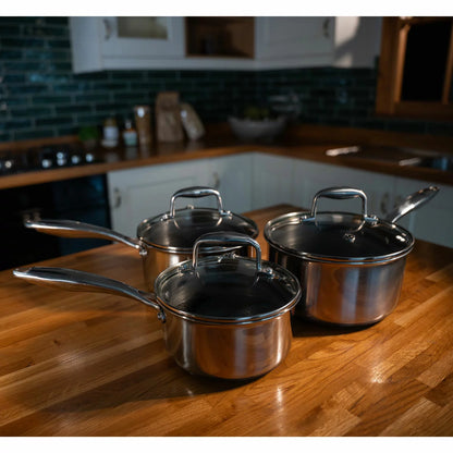 A high-end kitchen display featuring the PRO STEEL Fusion 6 piece saucepan set, showcasing the sleek stainless steel exteriors, glass lids, and the durable hybrid cooking surfaces.
