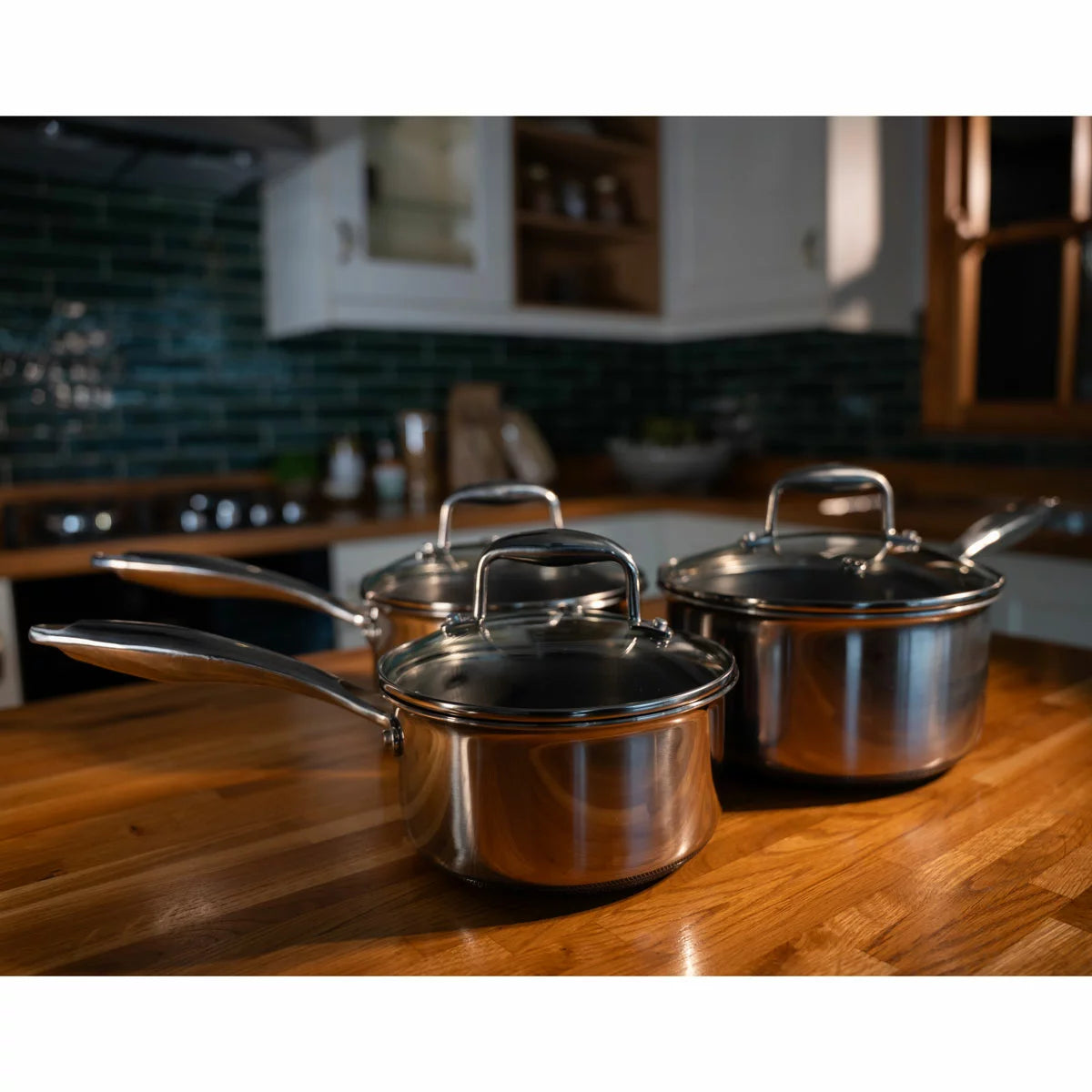 A high-end kitchen display featuring the PRO STEEL Fusion 6 piece saucepan set, showcasing the sleek stainless steel exteriors, glass lids, and the durable hybrid cooking surfaces.