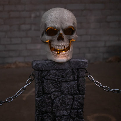 Pair of grey stone-effect Halloween skull fence sets with glowing LED eyes and linking chains anchored into a dark front lawn at dusk.