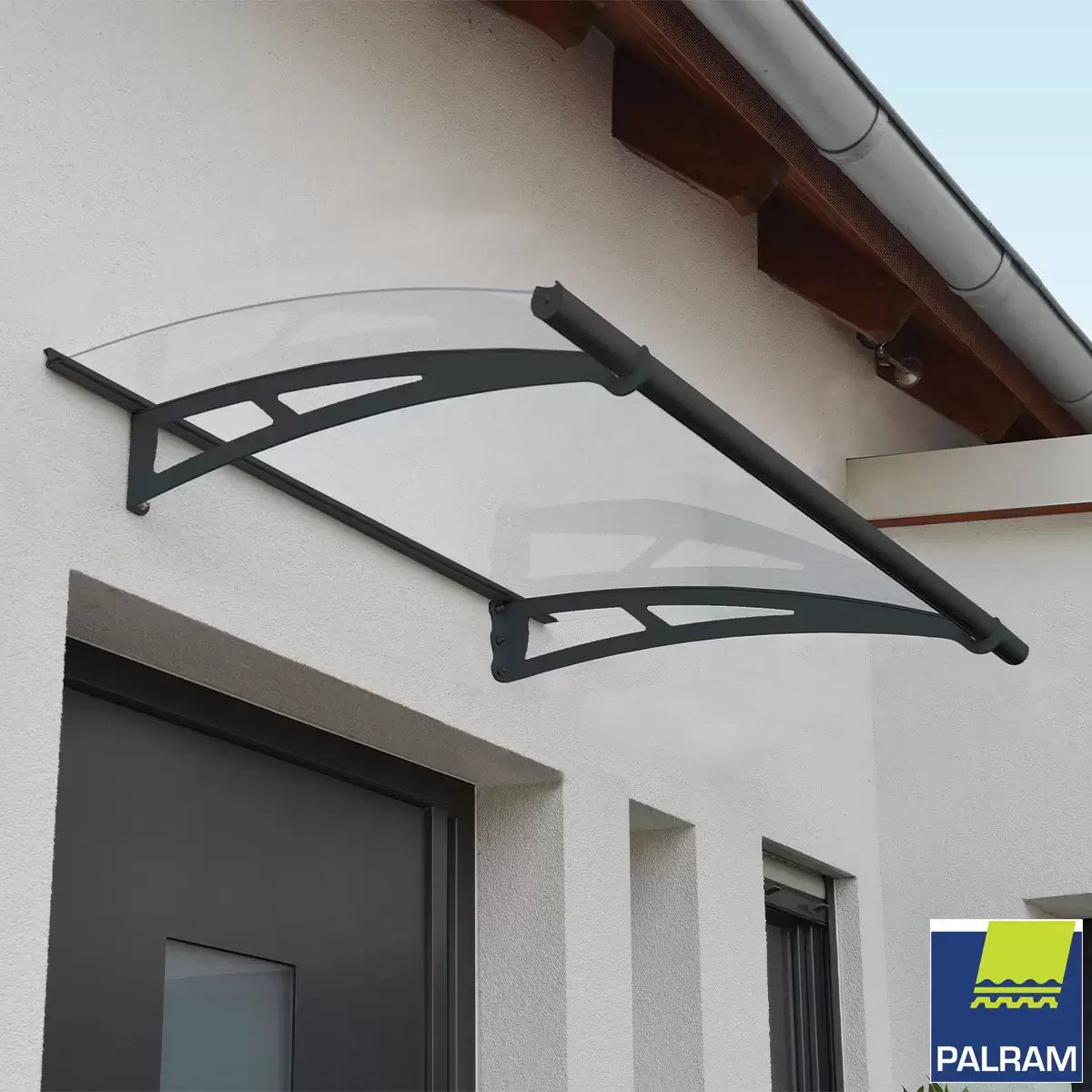 Angle view of a clear Palram Canopia Aquila 1500 door canopy with dark grey steel arms mounted over a residential front entrance.