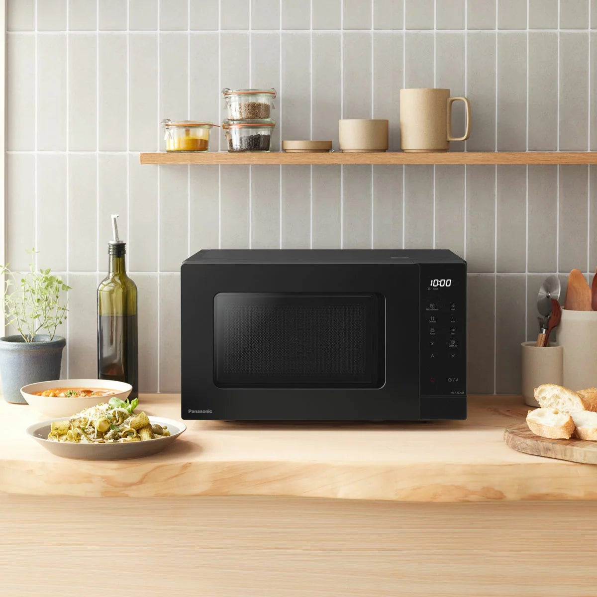 Front angle shot of the sleek black Panasonic 20L Solo Microwave NN-ST22QBBPQ sitting on a modern kitchen countertop with its digital LCD display illuminated.