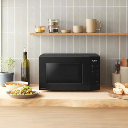 Front angle shot of the sleek black Panasonic 20L Solo Microwave NN-ST22QBBPQ sitting on a modern kitchen countertop with its digital LCD display illuminated.