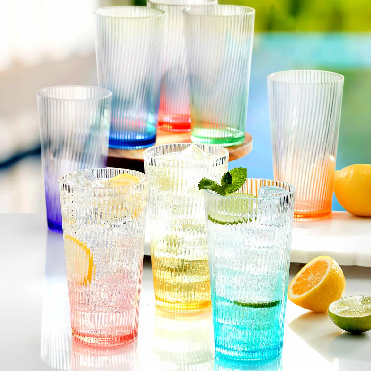 A set of eight Pandex ribbed acrylic tumblers with a vibrant ombre color gradient, arranged on an outdoor patio table, showcasing their elegant design and high-capacity size.