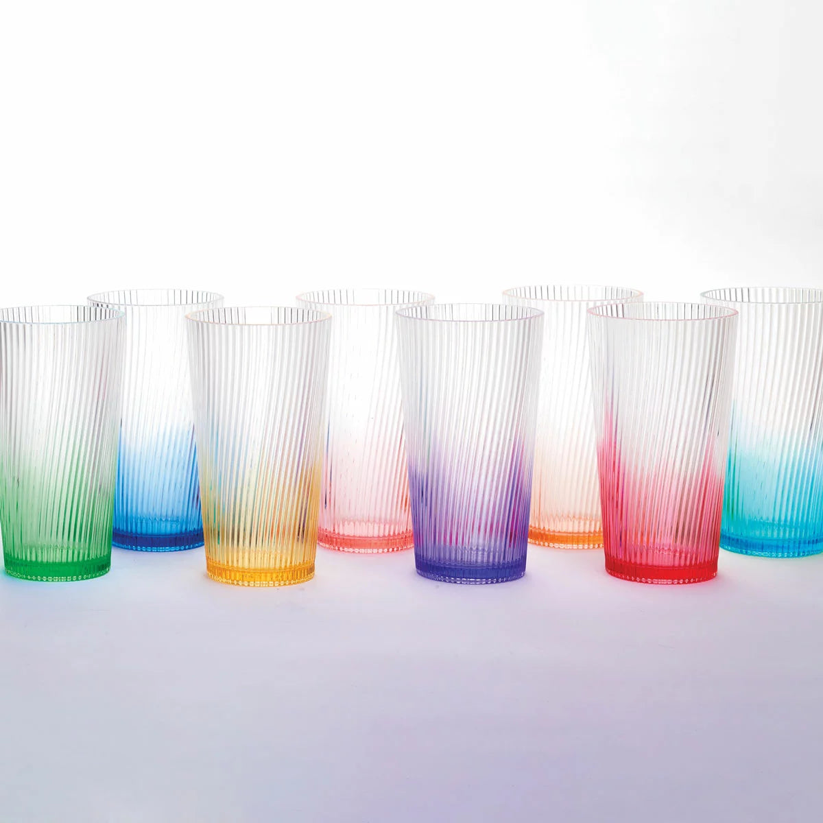 A set of eight Pandex ribbed acrylic tumblers with a vibrant ombre color gradient, arranged on an outdoor patio table, showcasing their elegant design and high-capacity size.