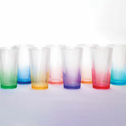 A set of eight Pandex ribbed acrylic tumblers with a vibrant ombre color gradient, arranged on an outdoor patio table, showcasing their elegant design and high-capacity size.