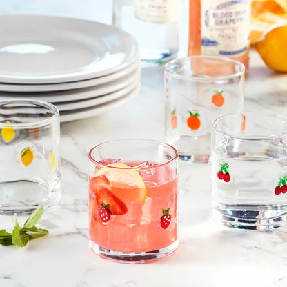 A set of four Pandex Spring Icon drinking glasses featuring vibrant Lemon, Orange, Cherry, and Strawberry illustrations, arranged on a sunlit wooden table.