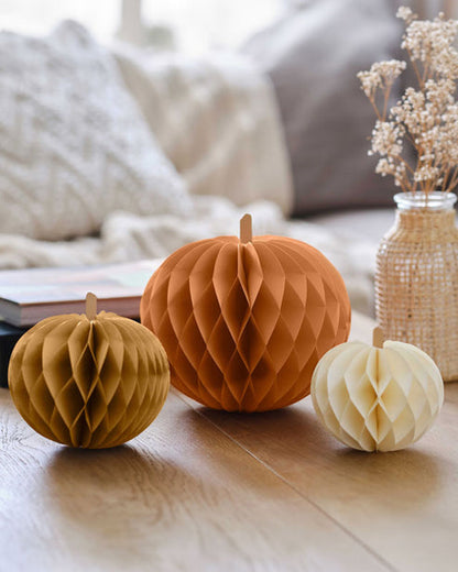 Three colorful paper pumpkin honeycomb decorations in four, five, and seven-inch sizes displaying magnetic closures on a wooden table.