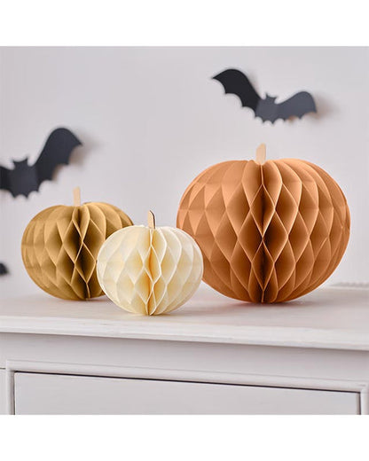 Three colorful paper pumpkin honeycomb decorations in four, five, and seven-inch sizes displaying magnetic closures on a wooden table.
