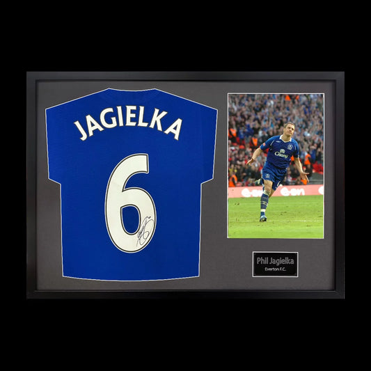 A professionally framed official Everton football shirt signed by Phil Jagielka, displayed with a crisp black mount inside a sleek wooden frame.