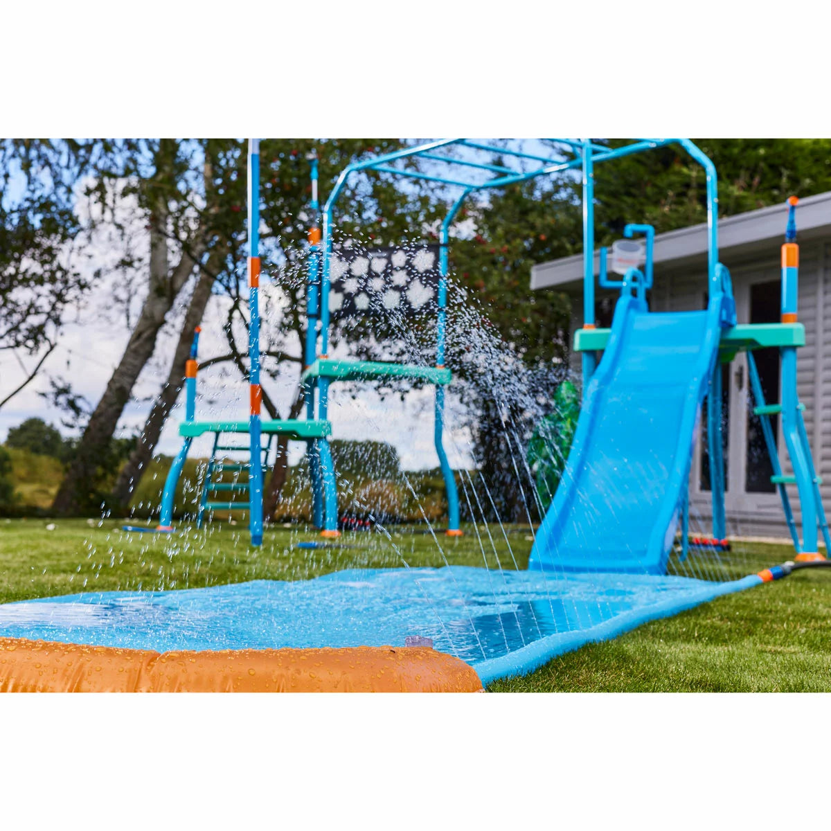 Plum Water Park Blaster Course blue outdoor play centre with climbing frame, water slide, sprinklers, monkey bars, and splash features installed in a garden for children's summer water fun-2