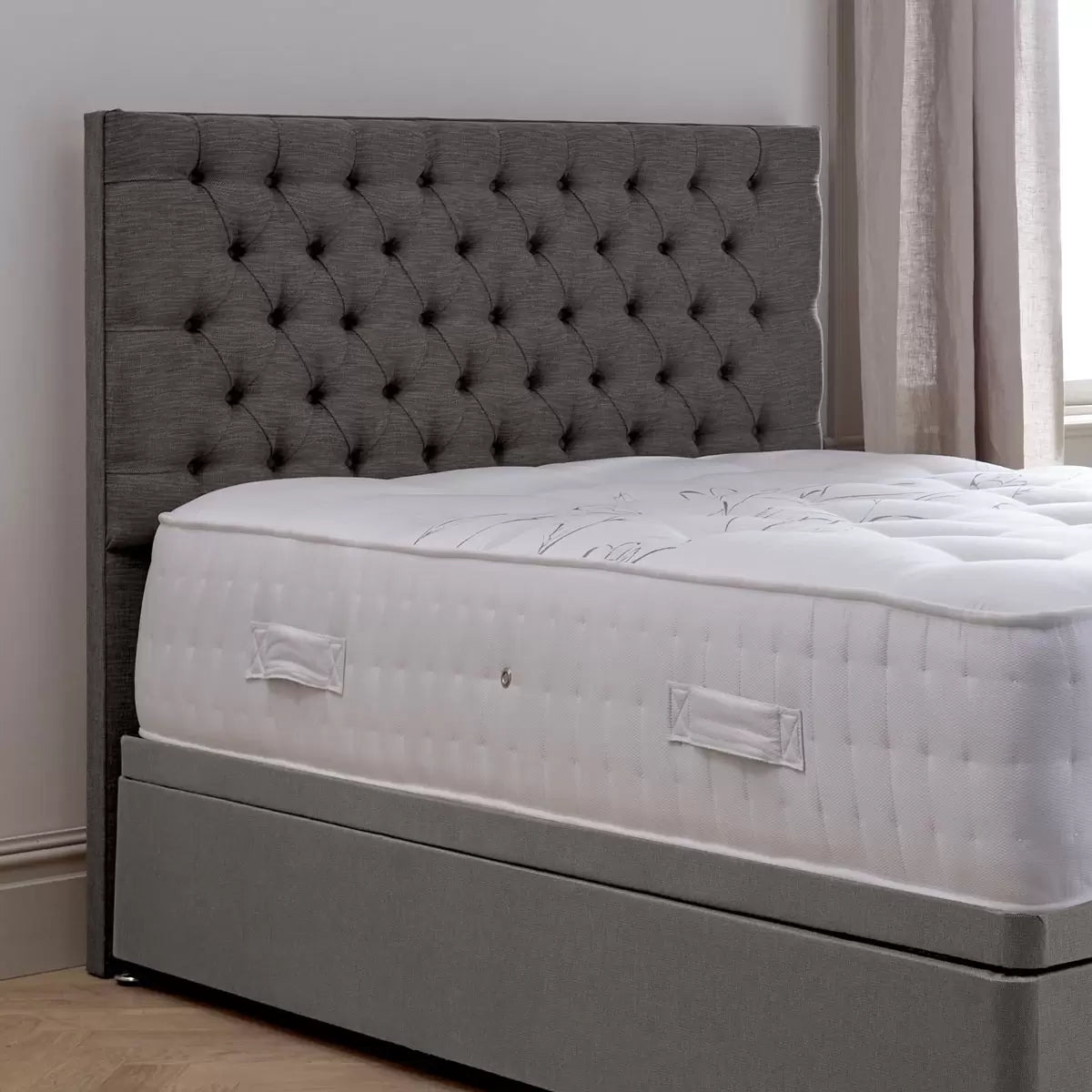Front view of the floor-standing Pocket Spring Bed Company Ravello headboard upholstered in deep plush grey Chesterfield buttoned fabric mounted behind a dressed divan bed.