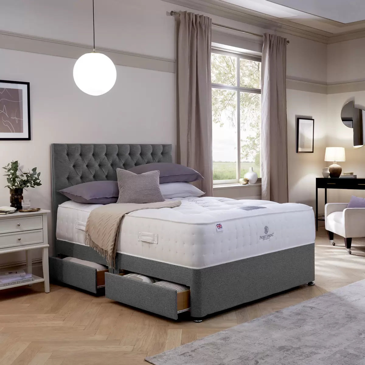 Front view of the floor-standing Pocket Spring Bed Company Ravello headboard upholstered in deep plush grey Chesterfield buttoned fabric mounted behind a dressed divan bed.