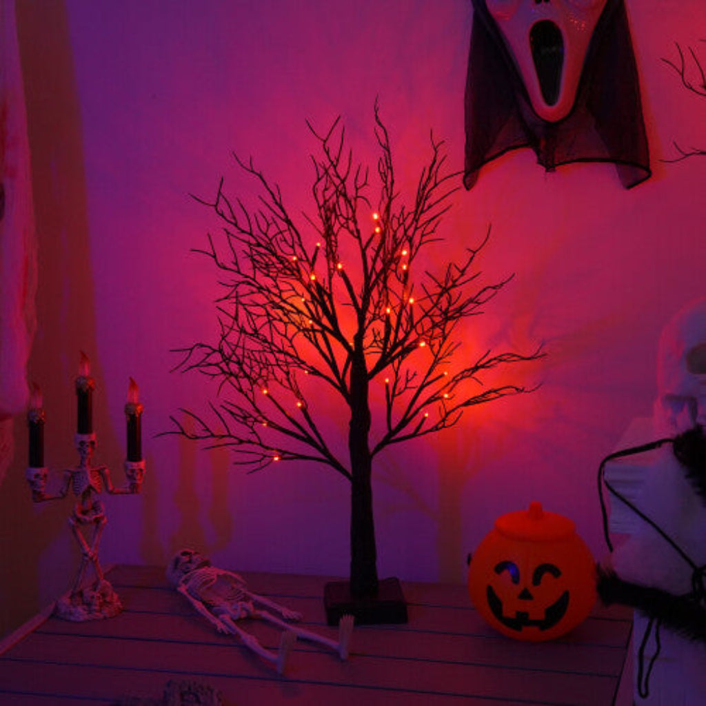 A pre-lit black birch tree with 24 warm LED lights glowing softly on an indoor mantelpiece decorated for Halloween