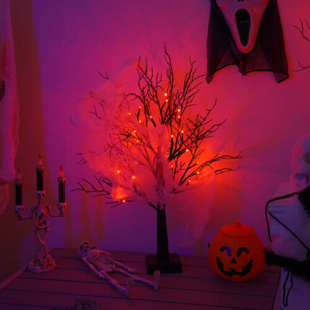 A pre-lit black birch tree with 24 warm LED lights glowing softly on an indoor mantelpiece decorated for Halloween