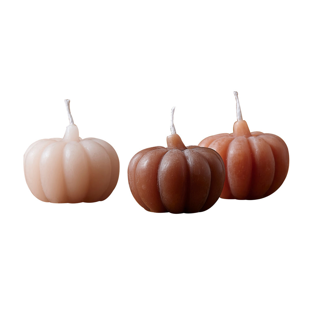 Three orange pumpkin shaped candles with detailed ribbed wax textures displayed on a dark wooden table beside rustic autumn leaves.