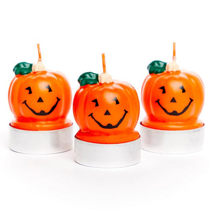 Three orange pumpkin-shaped tea light candles sitting on a dark wood table in warm candlelight setting.