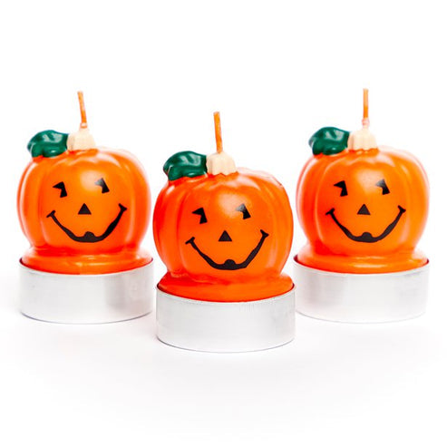 Three orange pumpkin shaped 5cm wax tea light candles arranged on a wooden rustic surface with a warm glowing flame.