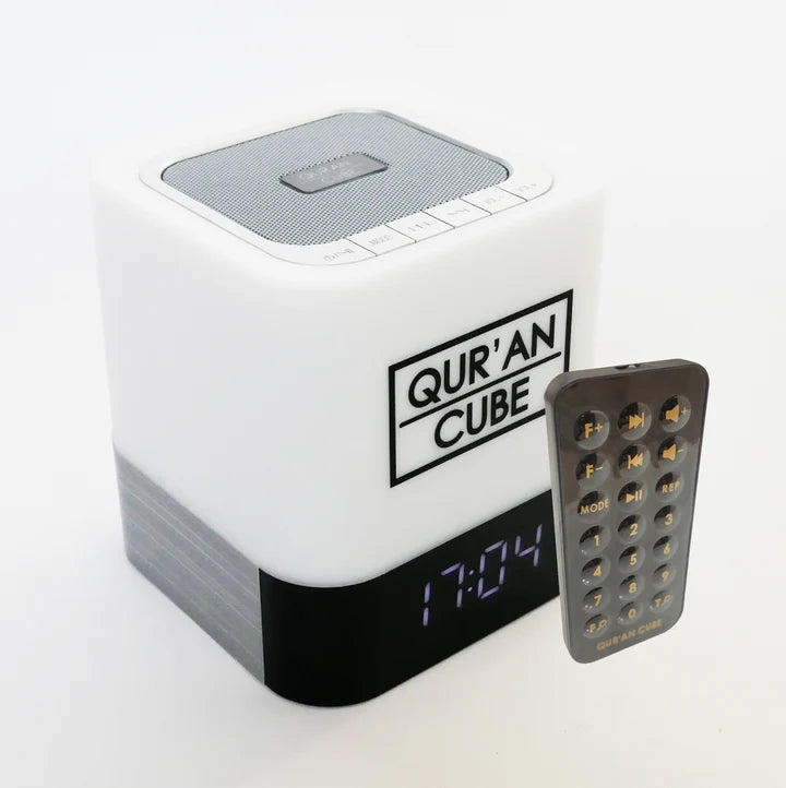 Studio shot of the rose gold Quran Cube LED X speaker glowing with a soft blue LED light on a bedside table displaying its digital clock face.