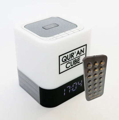 Studio shot of the rose gold Quran Cube LED X speaker glowing with a soft blue LED light on a bedside table displaying its digital clock face.
