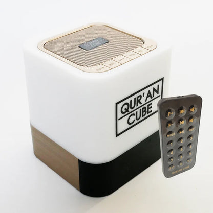 Studio shot of the rose gold Quran Cube LED X speaker glowing with a soft blue LED light on a bedside table displaying its digital clock face.