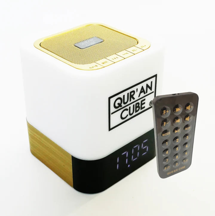Studio shot of the rose gold Quran Cube LED X speaker glowing with a soft blue LED light on a bedside table displaying its digital clock face.