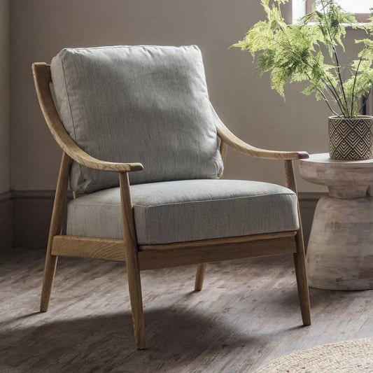 A side angle view of the Gallery Reliant natural linen armchair highlighting its exposed light-toned ash wood frame, padded natural linen upholstery, and retro silhouette.