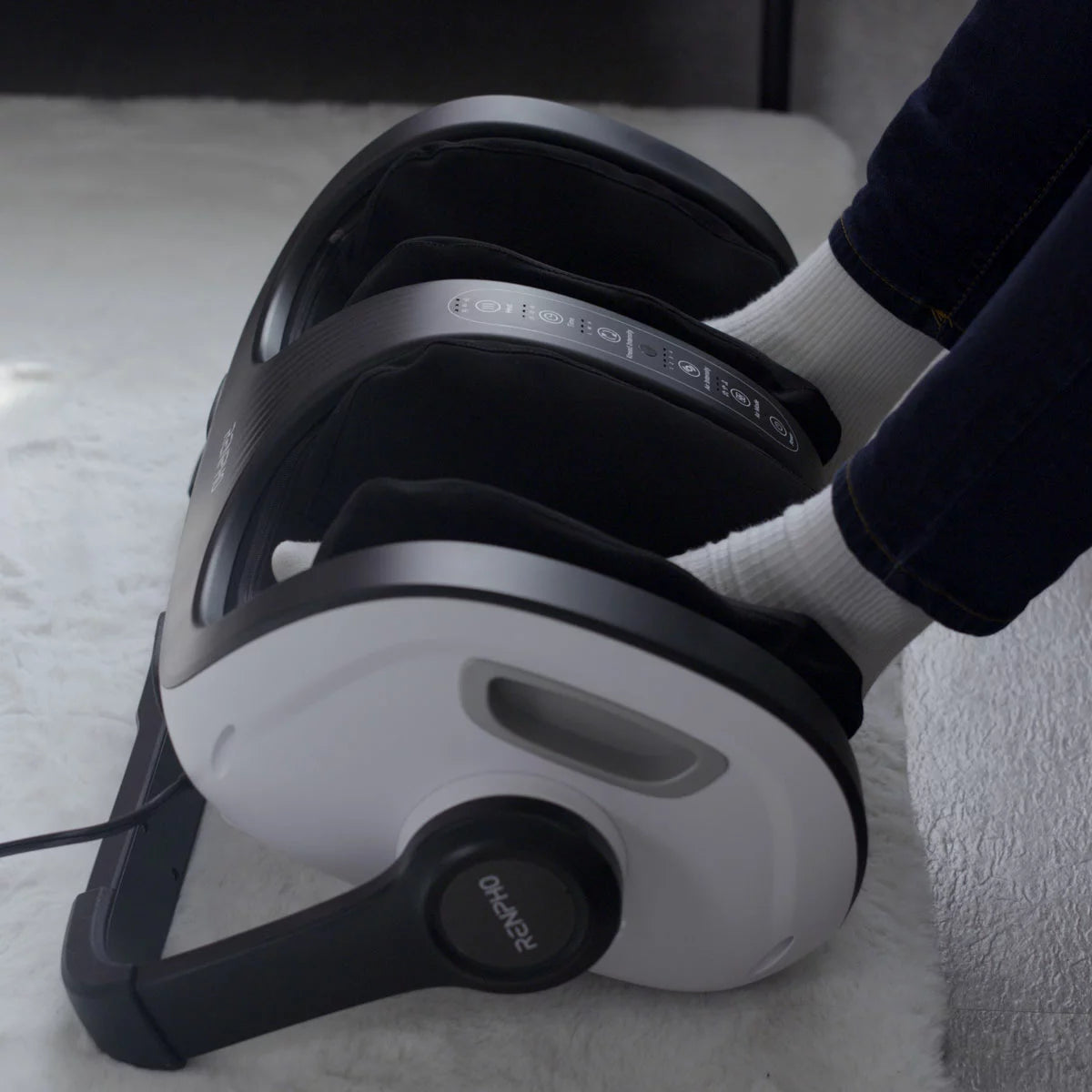 The Renpho 2-in-1 foot and calf massager in white, showcasing its ergonomic design and magnetic remote control set against a modern living room floor.