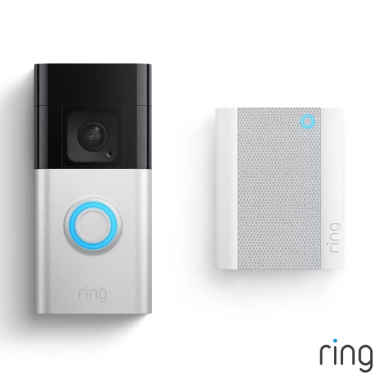 A front door installation showcasing the satin nickel Ring Battery Video Doorbell Plus mounted next to a dark wood frame, alongside the white Chime Pro plugged into a hallway wall outlet indoors.