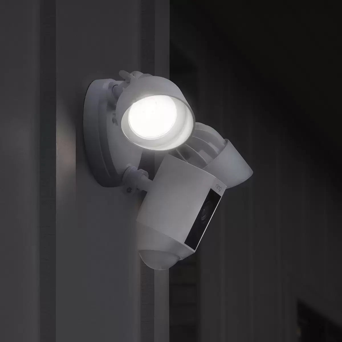 A pair of white Ring Floodlight Cam Plus units mounted on a clean exterior brick wall, showing the dual adjustable LED panels and central camera lens.