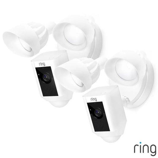 A pair of white Ring Floodlight Cam Plus units mounted on a clean exterior brick wall, showing the dual adjustable LED panels and central camera lens.