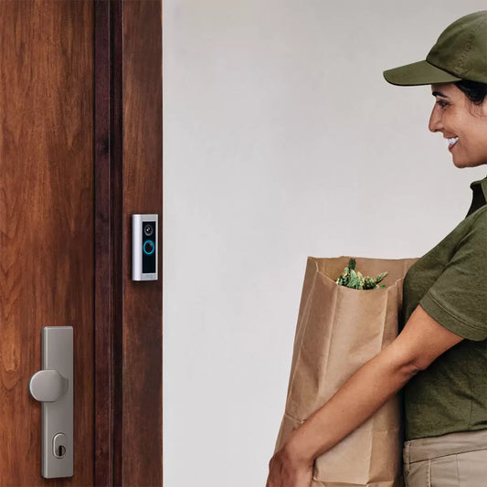 A sleek, satin nickel Ring Video Doorbell Pro 2 mounted vertically next to a modern front door, paired with a white Chime Pro plugged into a standard wall outlet.