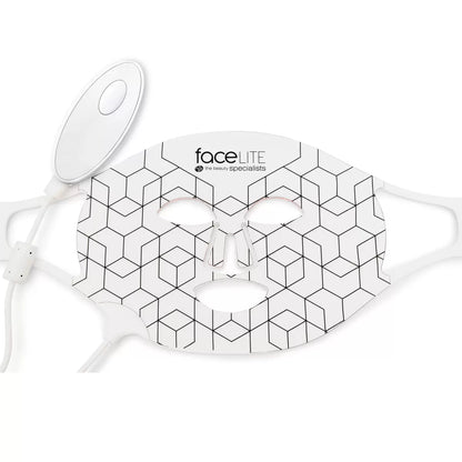 A flexible, white Rio faceLite silicone LED face mask shown glowing with soft red interior lights, resting flat on a contemporary vanity table next to its USB charging cord.