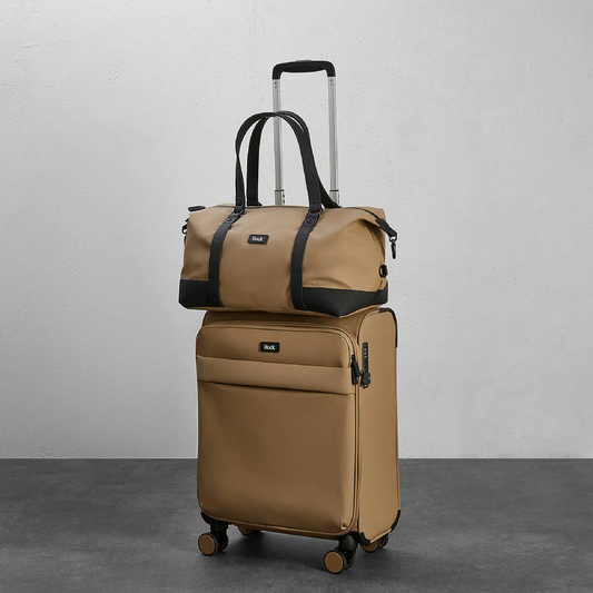 Front perspective view of the navy blue Rock Harper softside cabin suitcase paired with its matching under-seat holdall attached to the telescopic handle in an airport lounge.