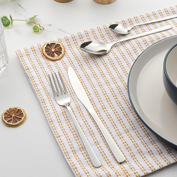 Top-down view of the 16-piece Russell Hobbs Vienna stainless steel cutlery set arranged neatly on a dark wooden dining table showcasing its mirror-polished reflective finish.